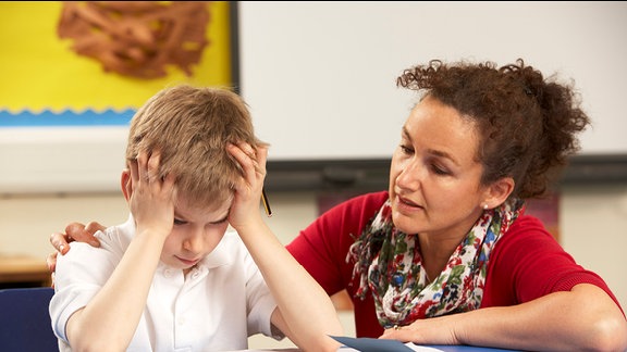 Ein Schüler sitzt mit einer Lehrerein am Tisch.