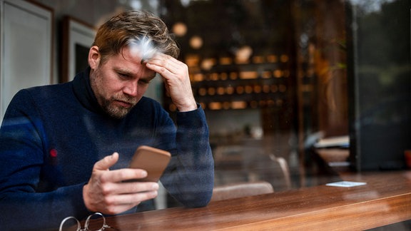 Mann schaut nachdenklich auf sein Handy