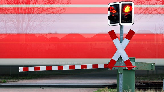 Zug passiert Bahnübergang mit Schranke.