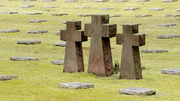 Drei Steinkreuze und Grabplatten auf einem Soldatenfriedhof