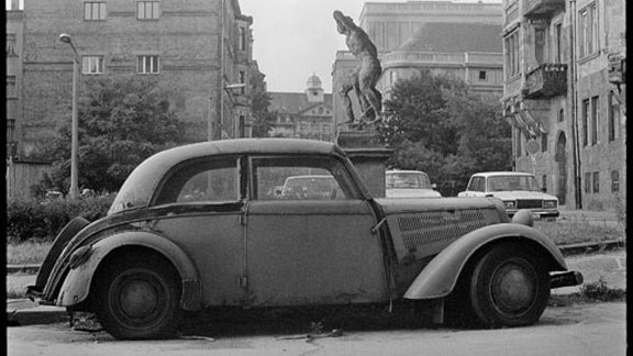 Ein völlig alter und kaputter Wartburg vor einer Statue.