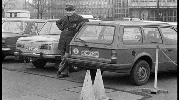 Mann steht an Auto mit Verkehrshütchen davor.