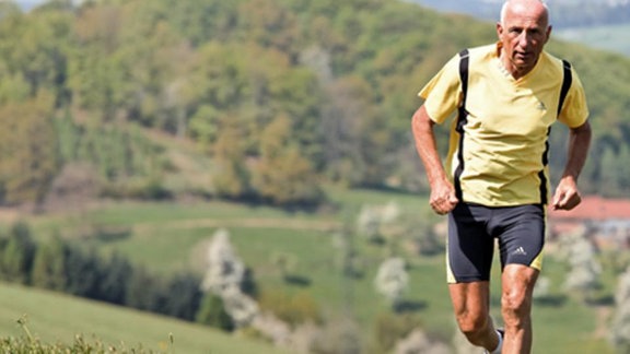 Ein Rentner joggt auf blühenden Bergwiesen.