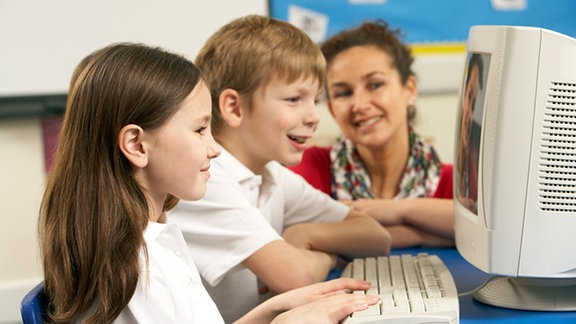 Zwei Kinder sitzen mit ihrer Mutter vor dem Computer.