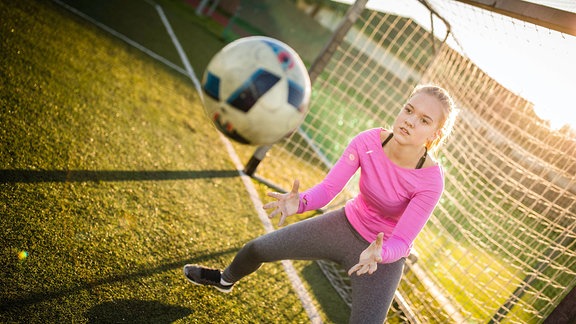 Teenager-Torhüterin, die einen Schuss während eines Fußballspiels fängt.