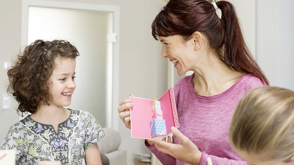 Kinder übereichen einer Frau ein Geschenk.