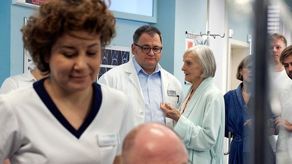 Im Krankenhausflur Hans-Peter Brenner (Michael Trischan, hi. li.) und seine Patientin Renate Harnack (Katharina Matz, hi. re.). Im Vordergrund Schwester Ulrike Stolze (Anita Vulesica, vorn)