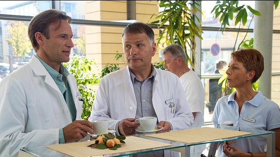 Dr. Stein, Dr. Heilmann und seine Frau Pia in der Cafeteria der Sachsenklinik.