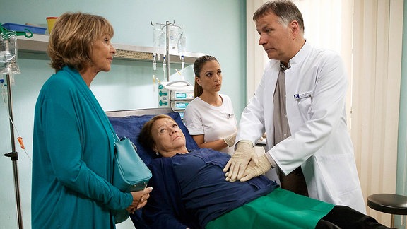 Regina Ströwe (Veronika Nowag-Jones, liegend) wurde mit starken Bauchschmerzen in die Sachsenklinik eingeliefert.  Dr. Roland Heilmann (Thomas Rühmann, re.) und Oberschwester Arzu (Arzu Bazman, 2.v.re.) untersuchen sie.