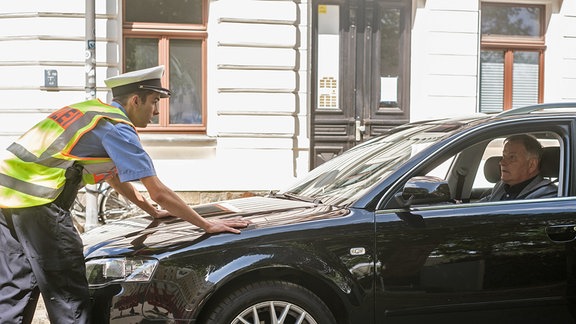 Ein Polizsit hat die Hände auf einer Motorhaube