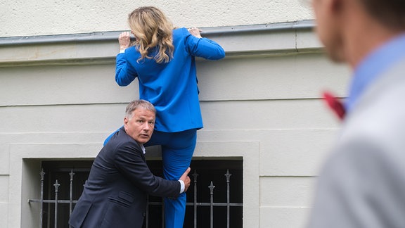 Roland und Sarah versuchen sich an einer Räuberleiter. Roland schaut erschrocken zu einem Mann, der die beiden beobachtet.