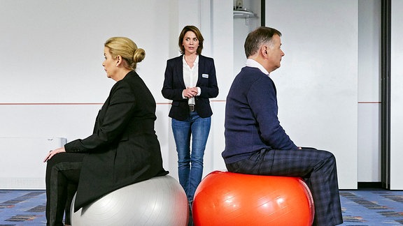 Sarah Marquardt (Alexa Maria Surholt, li.) und Roland Heilmann (Thomas Rühmann, re.) sutzen Rücken an Rücken auf Gymnastikbällen.