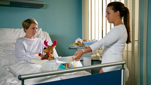 Schwester Julia (Sarah Tkotsch, re.) bringt Manuela Wüllner (Fanny Staffa, li.) ihr Essen, welches ab jetzt eine ärztliche Anordnung ist. Bei Manuela hat sich aufgrund ihrer schlechten Lebensführung eine Osteoporose entwickelt. Manuela nimmt in ihrem Leben alles schwerer als es ohnehin schon ist. Sie muss von den Menschen in ihrem Umfeld immer wieder motiviert werden, allen voran ihre Kollegin und Freundin Nadine. Doch die hat gerade richtig Mist gebaut