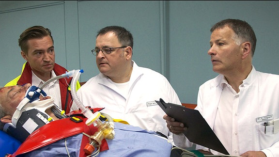 Nachdem Arzus Mutter überraschend in Leipzig vor der Tür ihrer Tochter stand, wird in die Sachsenklinik vom Notarzt (Markus Neumann, li.) ein Verletzter nach einem Autounfall eingeliefert. Dr. Roland Heilmann (Thomas Rühmann, re.) und Pfleger Hans-Peter Brenner (Michael Trischan, mi.) erkennen ihn sofort - Arzus Vater Klaus Ritter (Rolf Kanis, liegend).