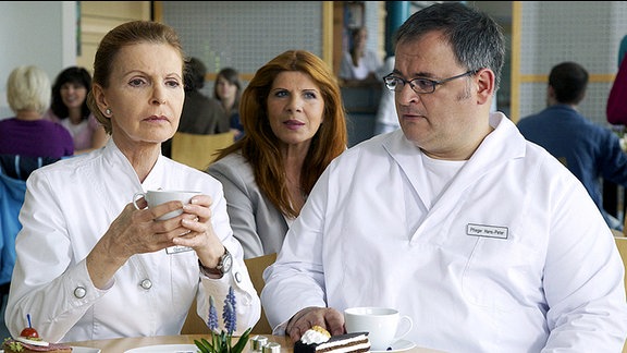 Oberschwester Ingrid (Jutta Kammann, li.) und Pfleger Hans-Peter Brenner (Michael Trischan, re.) unterhalten sich in der Cafeteria darüber, wie es zu dem Diebstahl der Medikamente gekommen sein kann. Sie sind verschlossen im Medikamentenschrank und nur wenige ausgewählte Personen haben für diesen Schrank einen Schlüssel. Leider bemerken die beiden nicht, dass ihr Gespräch belauscht wird - und zwar ausgerechnet von Dr. Vera Bader, die jede Gelegenheit nutzt, der Sachsenklinik zu schaden.