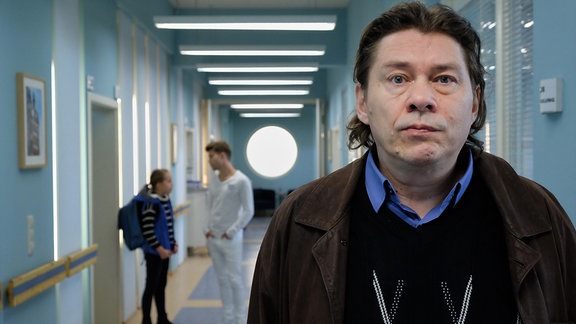 Michael Linse steht im Klinikgang. Im Hintergrund hört er Hanna hinter sich mit Pfleger Kris Haas plaudern.