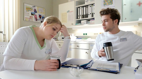 Miriam Schneider (Christina Petersen) und Kris Haas (Jascha Rust) sitzen an einem Tisch bei einer Tasse Kaffee.