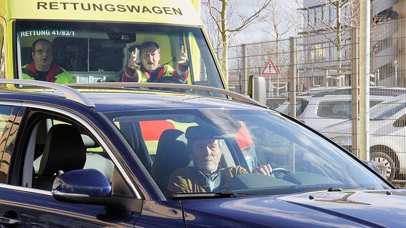 Als Dr. Henrik Oswald (Horst Janson, vorn) nach seinem Termin mit dem Auto wegfahren will, stößt er fast mit einem Rettungswagen zusammen.