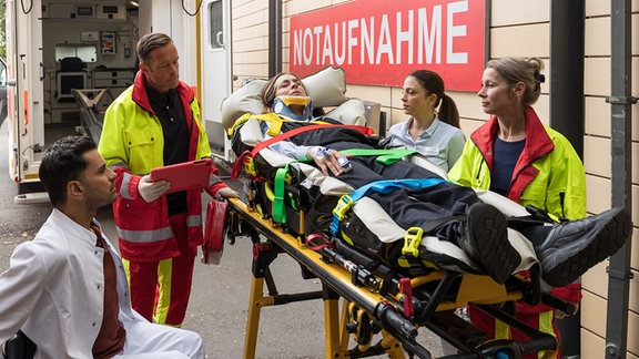 Susann Mess (Catherine Bode, liegend) wird vom Rettungsteam (Komparsen) in die Sachsenklinik eingeliefert. Die Busfahrerin hatte mit ihrem Bus einen Unfall. Auf Nachfragen von Arzu Ritter (Arzu Bazman, 2.v.re.) und Dr. Ilay Demir (Tan Caglar, li.) kann sich Susann Mess überhaupt nicht an den Unfallhergang erinnern.