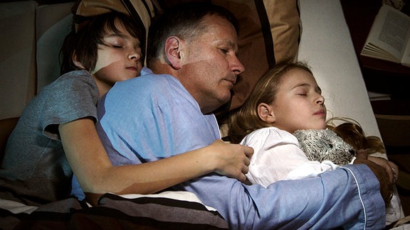 Familie Heilmann muss näher zusammenrücken. Pia verbringt die Nacht in der Sachsenklinik. Ihr soll am nächsten Tag ein Tumor aus der Brust entfernt werden. Die Kinder Jonas (Anthony Petrifke, li.) und Lisa (Ella Zirzow, re.) suchen nächtlich Schutz und Geborgenheit bei Roland (Thomas Rühmann, mi.).