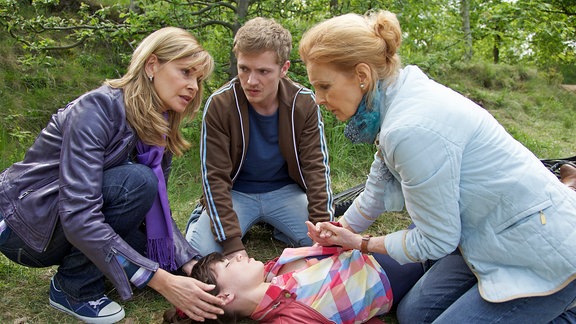 Oberschwester Ingrid (Jutta Kammann, re.) und Schwester Yvonne (Maren Gilzer, li.) treffen bei einem Waldspaziergang Ulli Scherer (Niklas Osterloh, mi.). Seine Freundin ist einfach von ihrem Fahrrad gekippt und seitdem bewusstlos. Eine Erklärung hat Ulli dafür nicht - Ingrid schon: Sie erkennt in dem Mädchen Miriam Göbel (Lore Richter, liegend), eine langjährige Patientin von Dr. Heilmann. Ulli jedoch wüsste nicht, warum Miriam dauerhaft in Behandlung gewesen sein sollte.