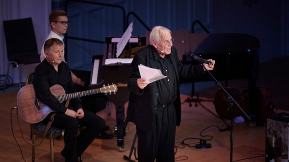 Rolf Becker auf der Bühne und Thomas Rühmann im Hintergrund an der Gitarre