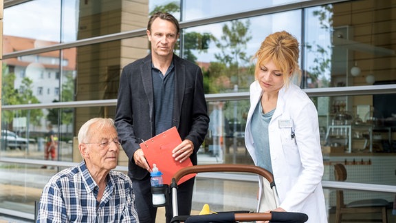 Dr. Ina Schulte (Isabell Gerschke, re.) trifft zufällig vor der Sachsenklinik auf Otto Stein (Rolf Becker, li.), der seine Urenkelin Klara dabei hat. Die beiden unterhalten sich angeregt. Als jedoch Dr. Martin Stein (Bernhard Bettermann, mi.) dazukommt, beendet Ina die Situation eilig.