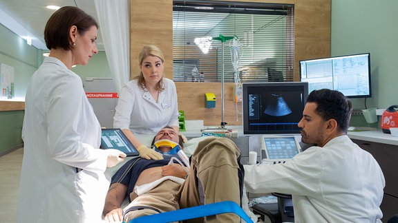 David Kaiderling (Sven Gerhardt, liegend), Chef einer kleinen Messebaufirma, wurde nach einem Sturz mit einer Pfählungsverletzung in die Sachsenklinik eingeliefert. Hier übernehmen Prof. Maria Weber (Annett Renneberg, li.), Dr. Ilay Demir (Tan Caglar, re.) und Krankenpflegerin Miriam Schneider (Christina Petersen, mi.).