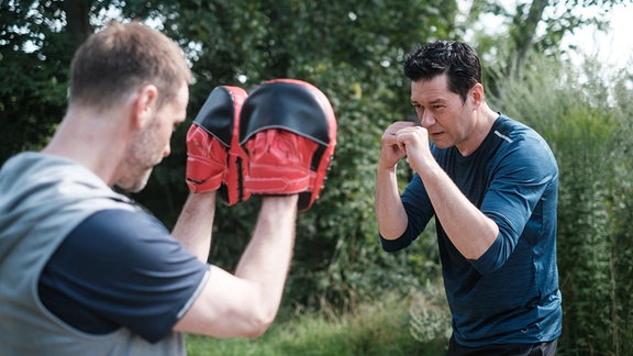 Dr. Brentano und Dr. Hoffmann boxen mit Trainingsausrüstung im Park