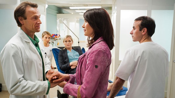 Antonia Bach (Claudia Mehnert, 2.v.re.) und  Dr. Martin Stein (Bernhard Bettermann, li.) halten Händchen. Im Hintergrund:  Nicole Lamprecht (Judith Hoersch, mi.) auf einer Krankenliege.