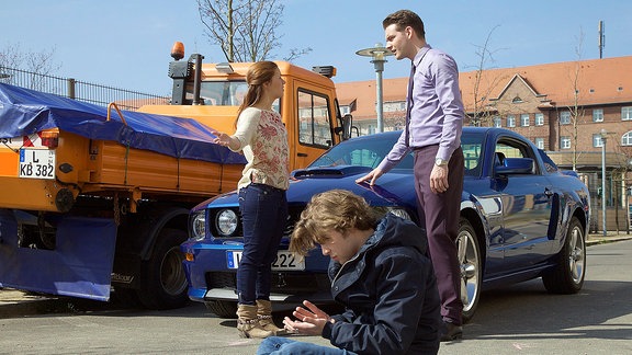 Szene aus "In aller Freundschaft - Folge 695": Clemens Manthey (Max König, re.) hat Kris Haas (Jascha Rust, vorn) mit seinem Auto angefahren. Schwester Julia Weiß (Sarah Tkotsch, li.) hat das Ganze beobachtet und stellt Clemens barsch zur Rede. Rechte: MDR/Wernicke