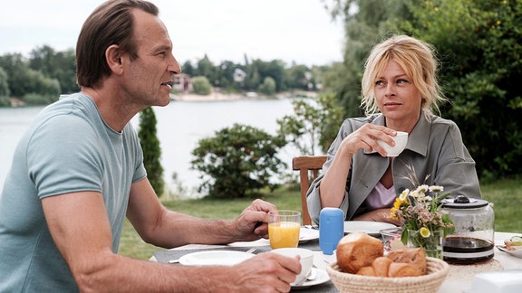 Dr. Stein und Dr. Schulte sitzen gemeinsam am Frühstückstisch auf einer Terrasse.