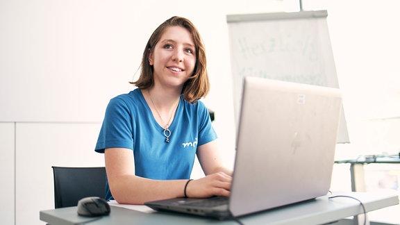 Eine junge Frau sitzt an einem Schreibtisch vor einem Laptop.