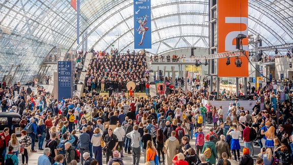 Buchmessechor von MDR KLASSIK auf der Leipziger Buchmesse 2024: Blick in die Glashalle mit dem MDR-Rundfunkchor und der Percussionistin Vivi Vassileva und der Dirigentin Julia Selina Blank.