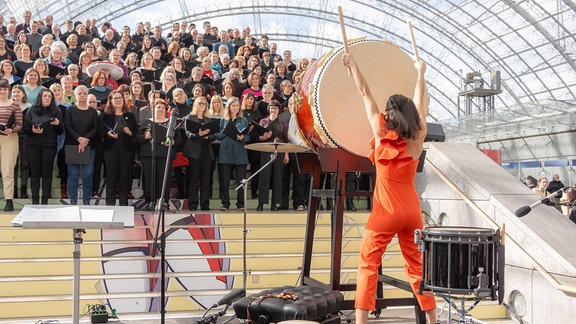 Buchmessechor von MDR KLASSIK auf der Leipziger Buchmesse 2024: Buchmessechor von MDR KLASSIK auf der Leipziger Buchmesse 2024: die Percussionistin Vivi Vassileva schlägt mit zwei großen Sticks auf deine große Trommel. 