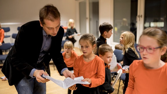 Dirigent Alexander Schmitt beugt sich mit Kindern des MDR-Kinderchors über Noten.