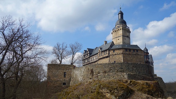 Blick auf Burg Falkenstein, die umgeben von einer Mauer auf einem Hügel liegt.