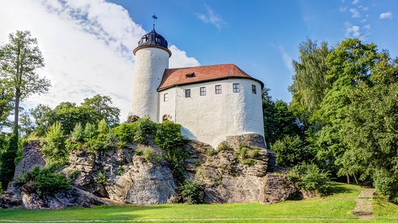 Burg Rabenstein in Chemnitz: ein weißes Gebäude mit einem Turm auf einer grünen Wiese.