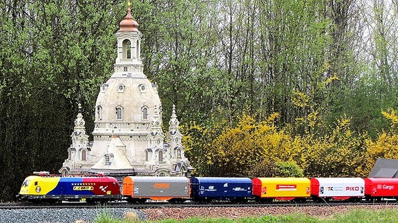 Eine bunte Modellbahn fährt an dem Modell der Frauenkirche vorbei.