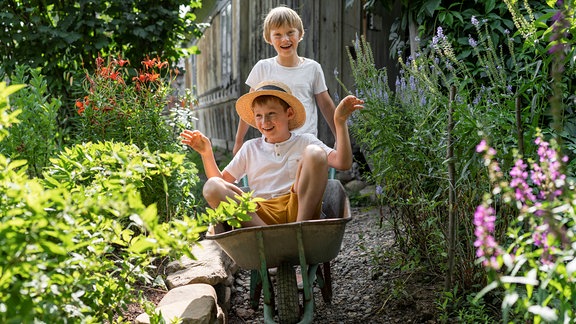 Kinder spielen mit einer Schubkarre im Garten.