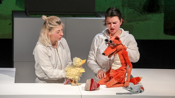 Aufführung des Stückes "Alle Seine Entlein" im Puppentheater Magdeburg. Man sieht zwei Frauen mit einer Fuchs-Puppe und einer Enten-Puppe auf der Bühne des Theaters. 