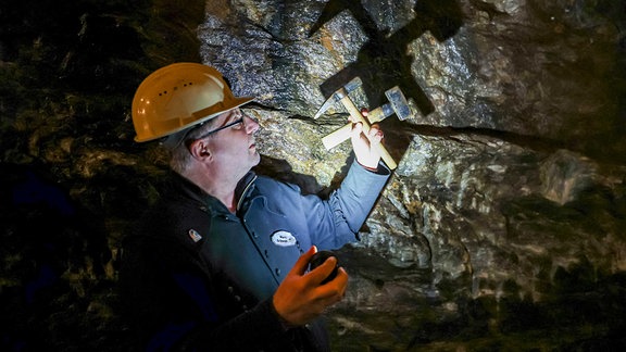 Marc Schwan (Vorstandsvorsitzender Verein Altbergbau "Markus-Röhling-Stolln") hält Schlägel und Eisen im Besucherbergwerk in die Höhe.