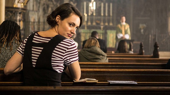 Szene aus der Serie "Fleabag", eine junge Frau sitzt in einer Kirchenbank und dreht sich um.