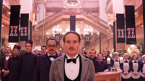 Szene aus dem Film "Grand Budapest Hotel", die Hotelangestellten stehen in der Eingangshalle und blicken in die Kamera