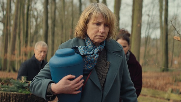 Schauspielerin Corinna Harfouch in einer Szene des Films "Sterben" im Wald mit einer blauen Urne.