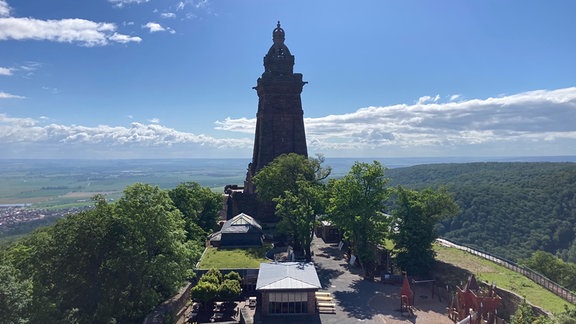 Skultptur zweier Mädchen vor Blumenrabatten und einem Turm