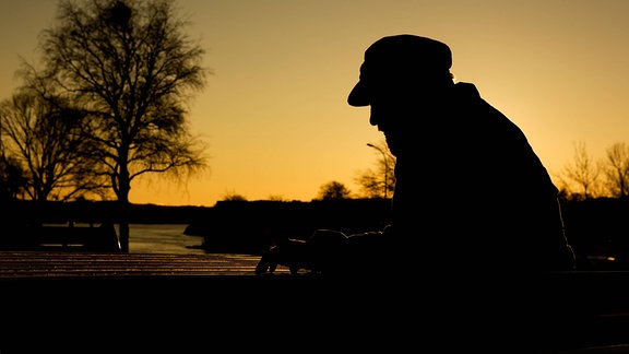 Themenbild Depression - Silhouette eines nachdenklichen Mannes im Gegenlicht der untergehenden Abendsonne