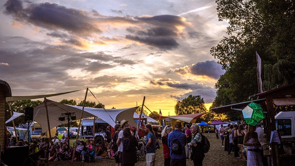 Menschen tanzen auf einem Festival im Freien bei Sonnenuntergang.