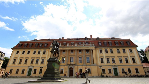 Barockgebäube mit gelblich gestrichener Fassade, Totale mit einem Reiterdenkmal im Vordergrund