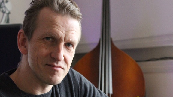 Portrait des Musikers, am Piano sitzend, im Hintergrund ein Contrabass